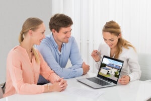 presentazione incarico immobiliare con consulente che mostra piano di vendita su laptop a coppia di venditori