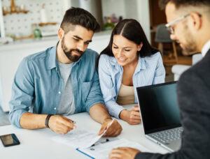 coppia che valuta l’agente immobiliare durante la firma dei documenti a un tavolo di consulenza