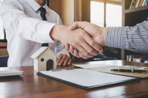 testimonianze venditori: stretta di mano tra agente e venditore con casa sul tavolo